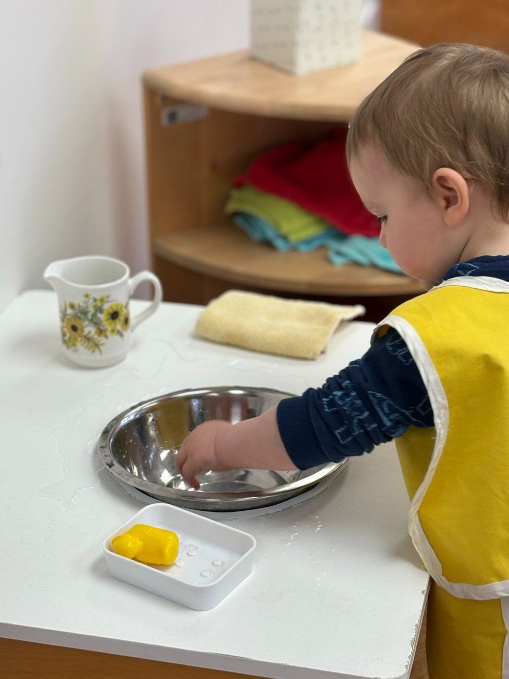 A young boy is playing with a bowl and soap on a table.