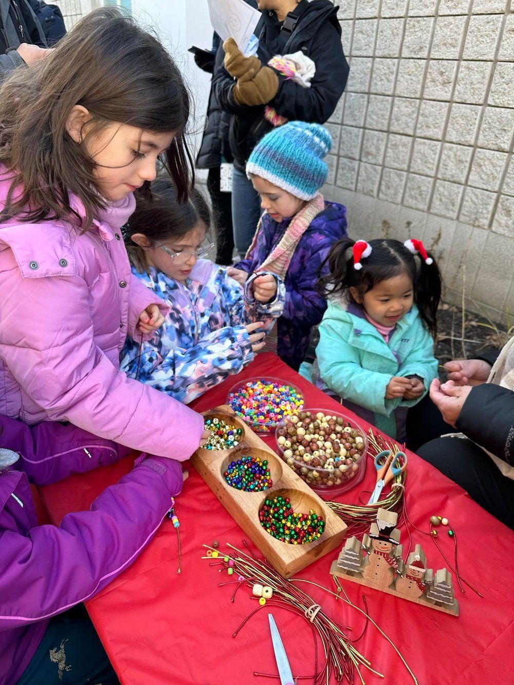 A group of young girls are sitting at a table playing with beads.
