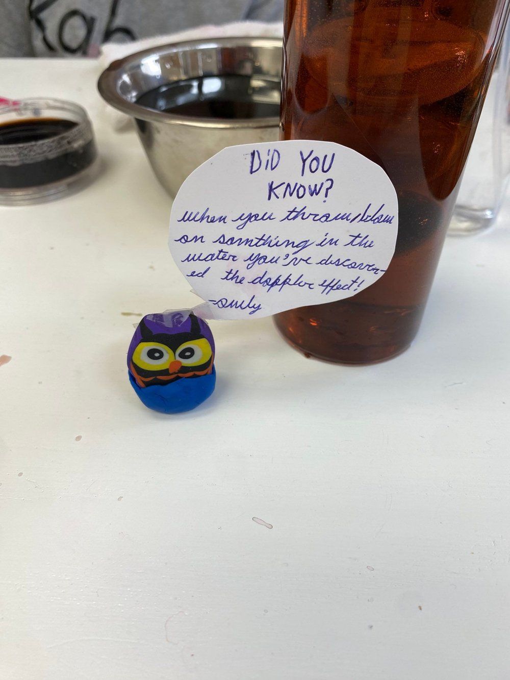 A small owl is sitting on a table next to a bottle of beer.