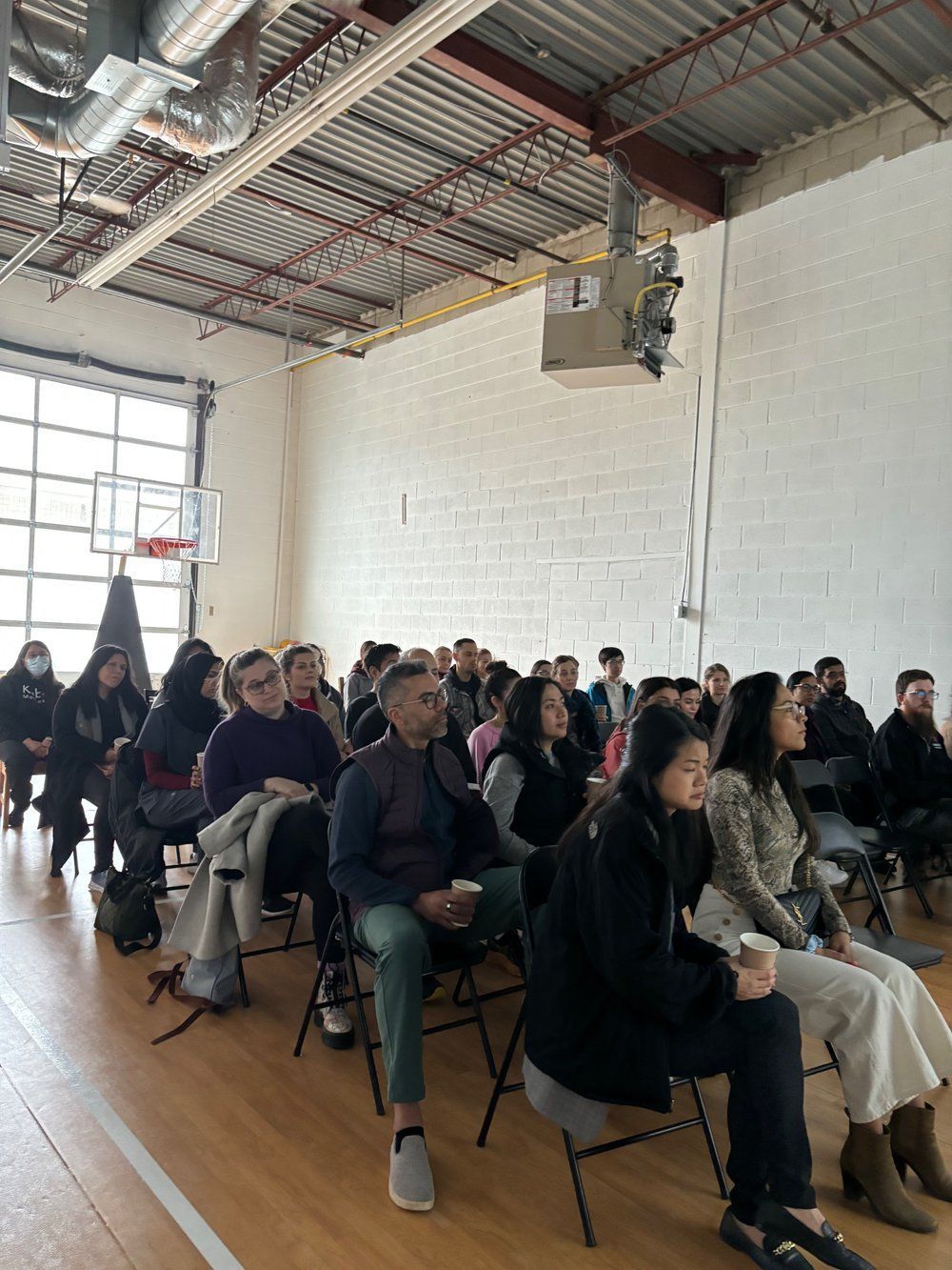 A group of people are sitting in chairs in a room with a basketball hoop in the background.