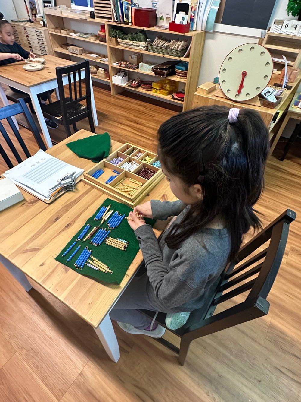 A little girl is sitting at a table in a classroom playing with toys.