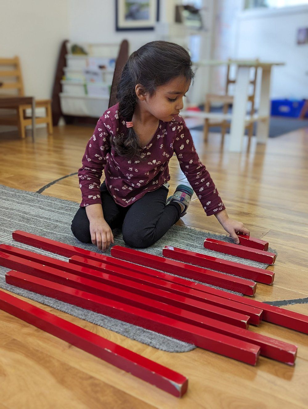 A little girl is sitting on the floor playing with red wooden sticks.