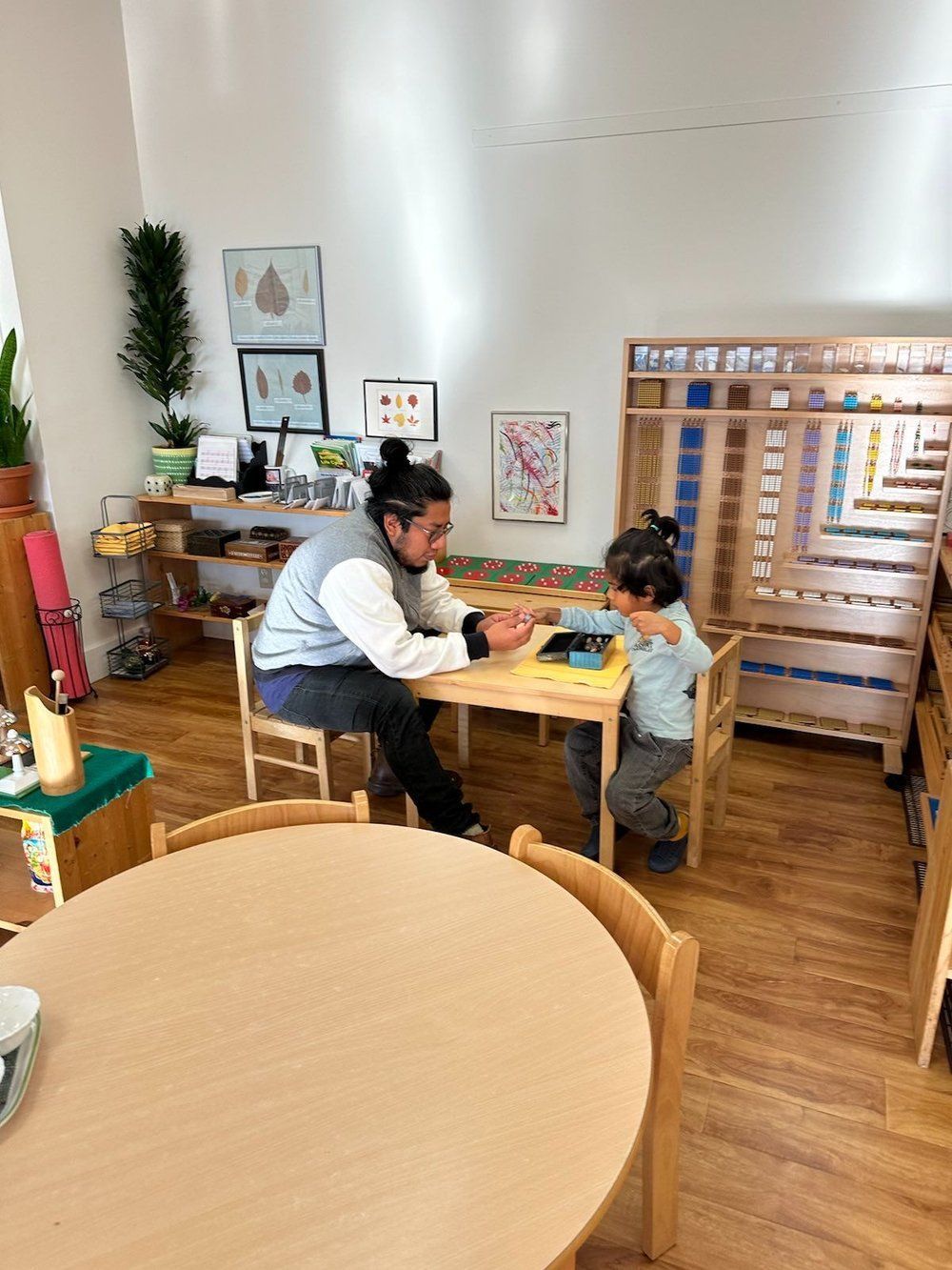 A woman is sitting at a table with a child in a classroom.