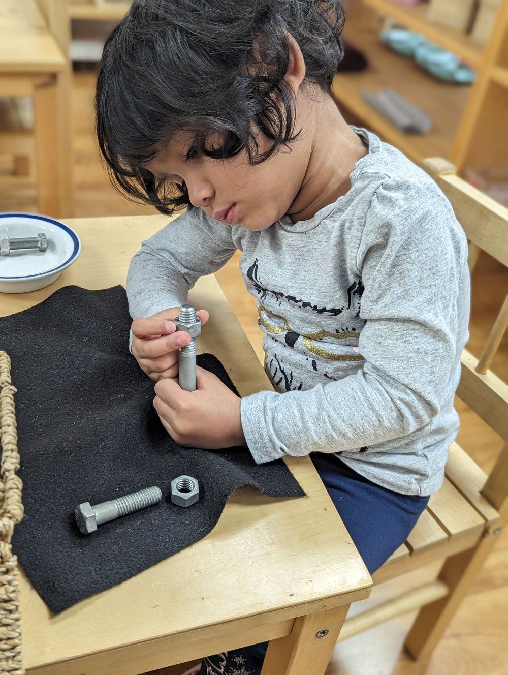 A young boy is sitting at a table playing with nuts and bolts.
