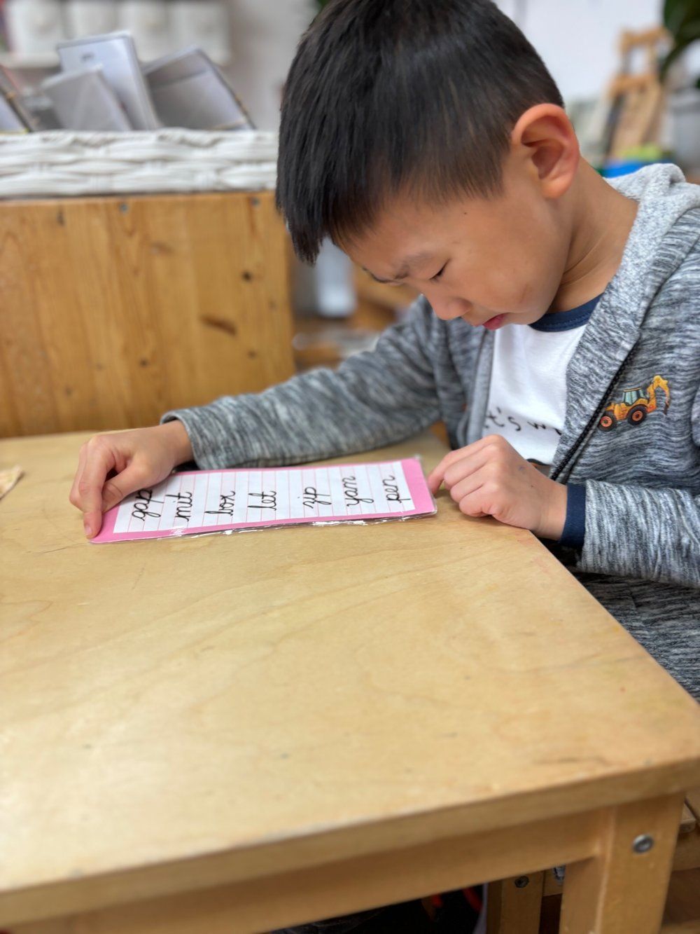 A young boy is sitting at a wooden table writing on a piece of paper.
