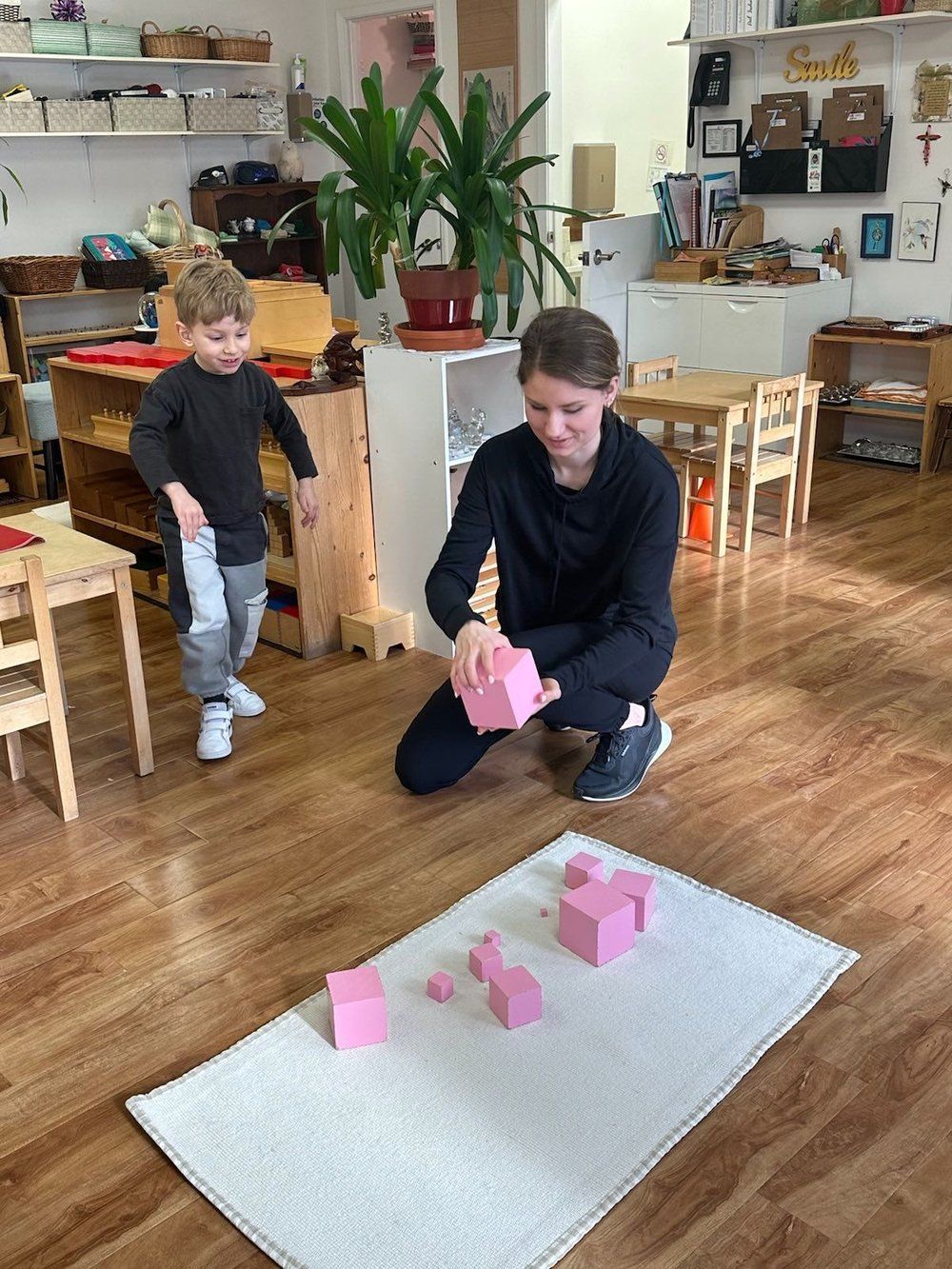 A woman and a child are playing with pink blocks in a classroom.
