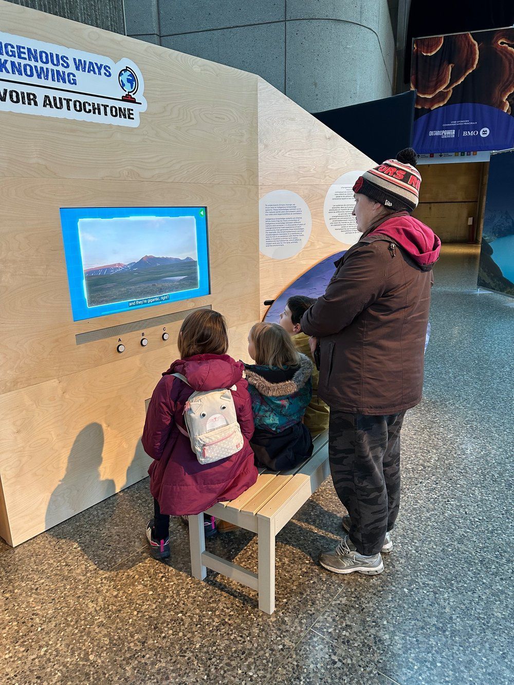A man and two children are sitting on a bench looking at a screen.