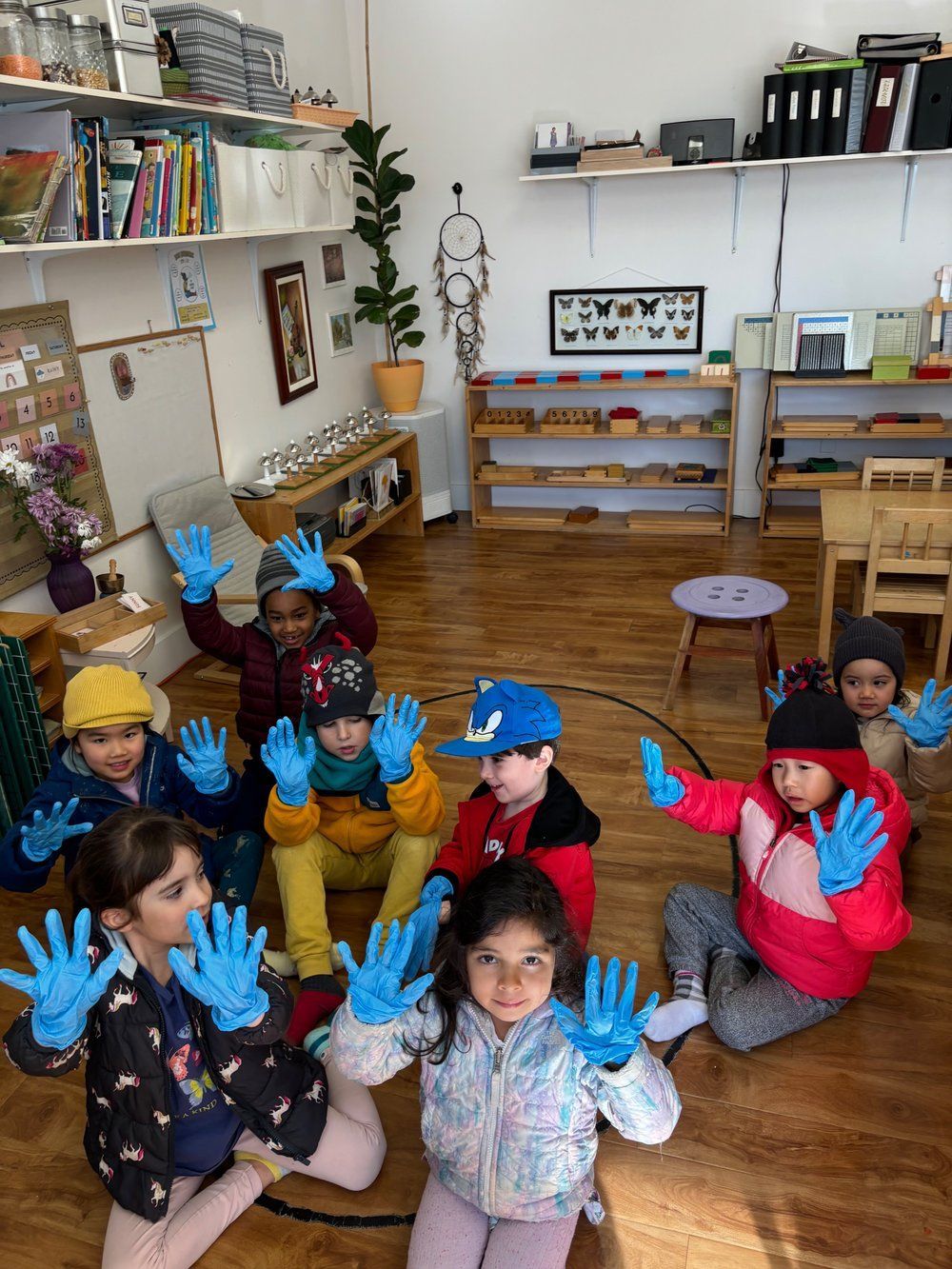 A group of children wearing blue gloves are sitting on the floor.