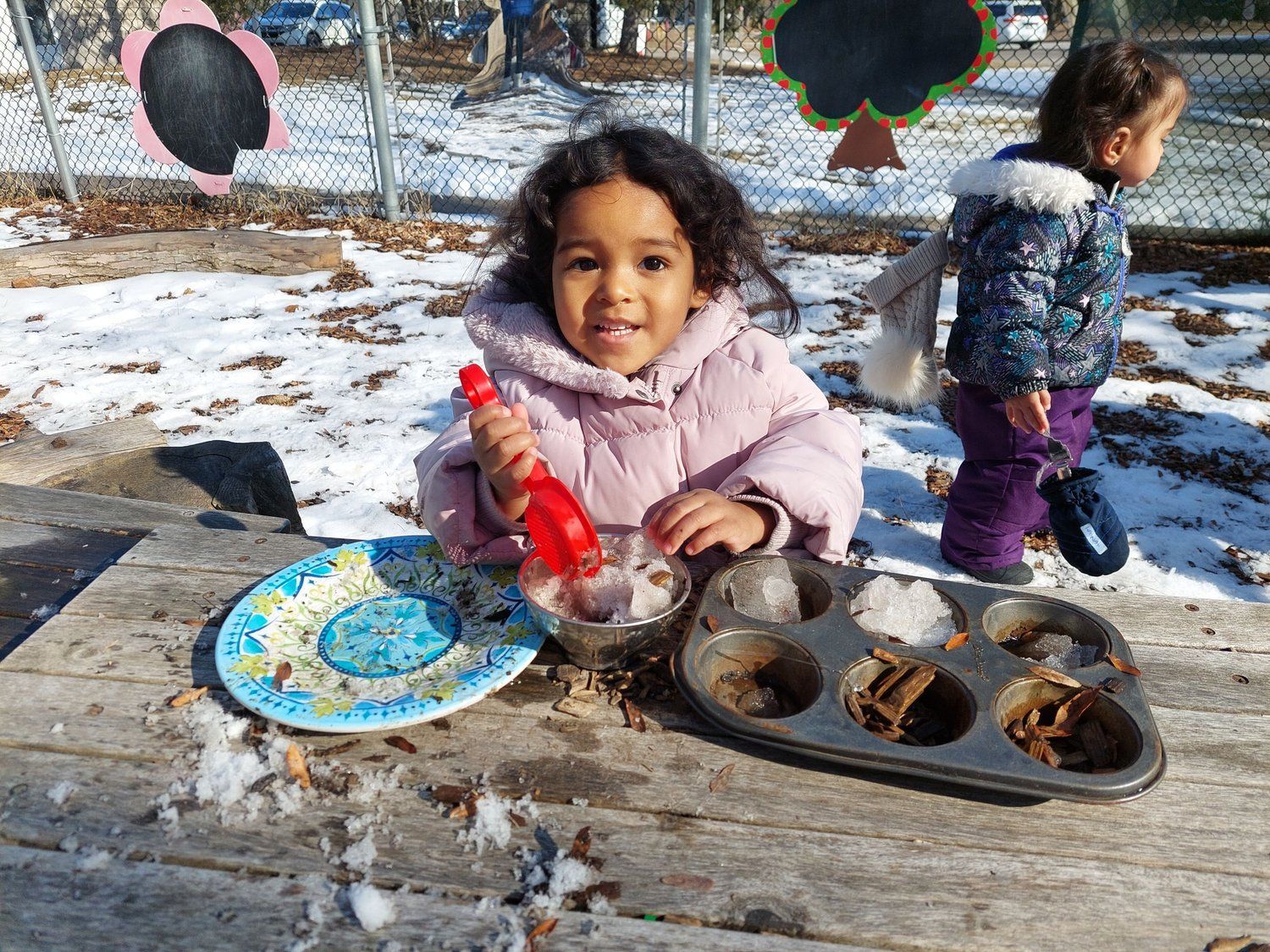 A little girl is sitting at a table with plates and ice cubes.