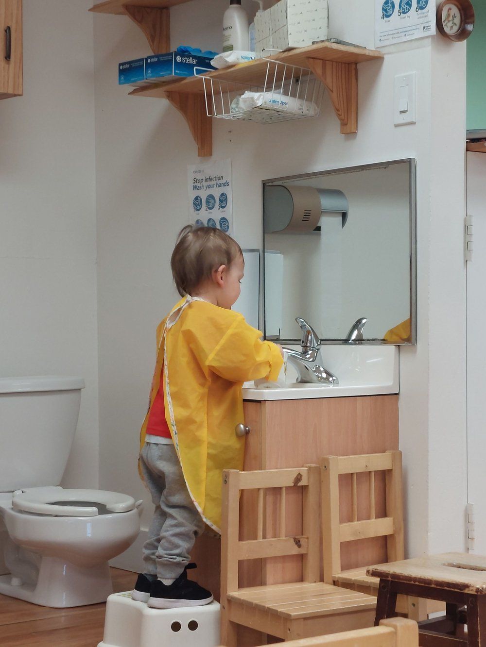 A child in a yellow apron is standing in front of a sink in a bathroom