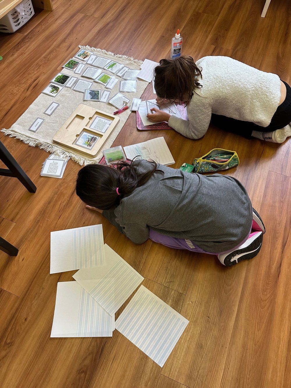 Two children are laying on the floor writing on papers.