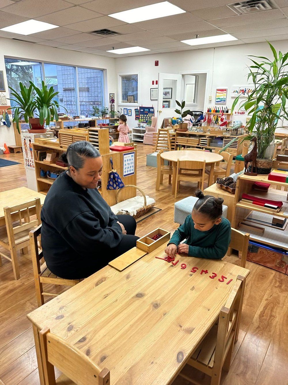 A man and a girl are sitting at a wooden table in a classroom.