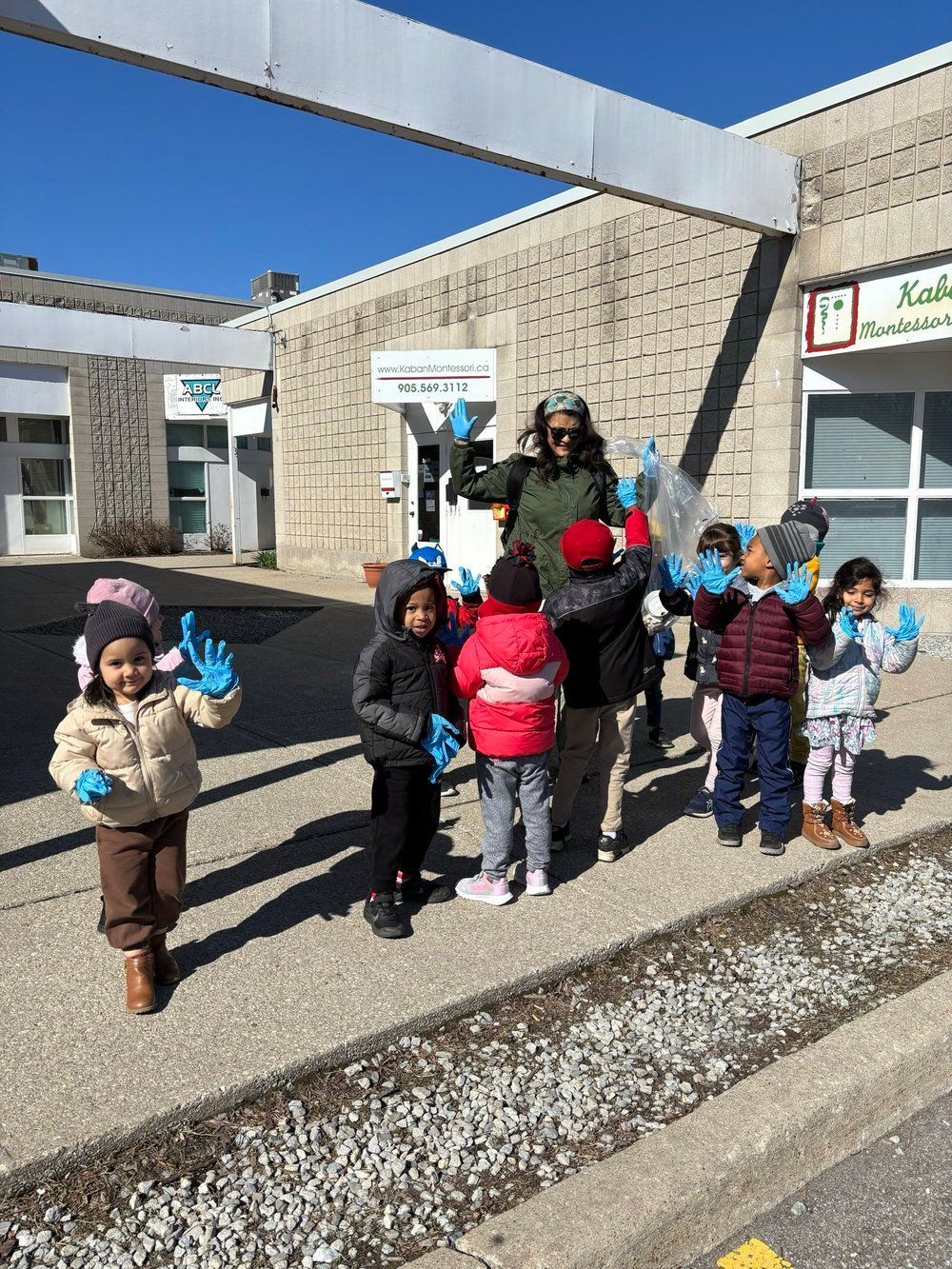 A group of children wearing blue gloves are standing in front of a building.