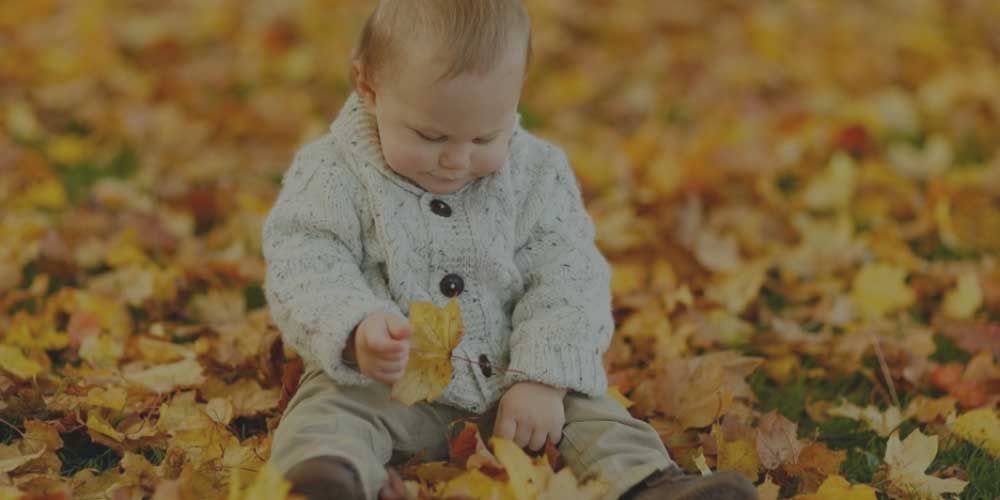 A montessori child is sitting in a pile of leaves holding a leaf.