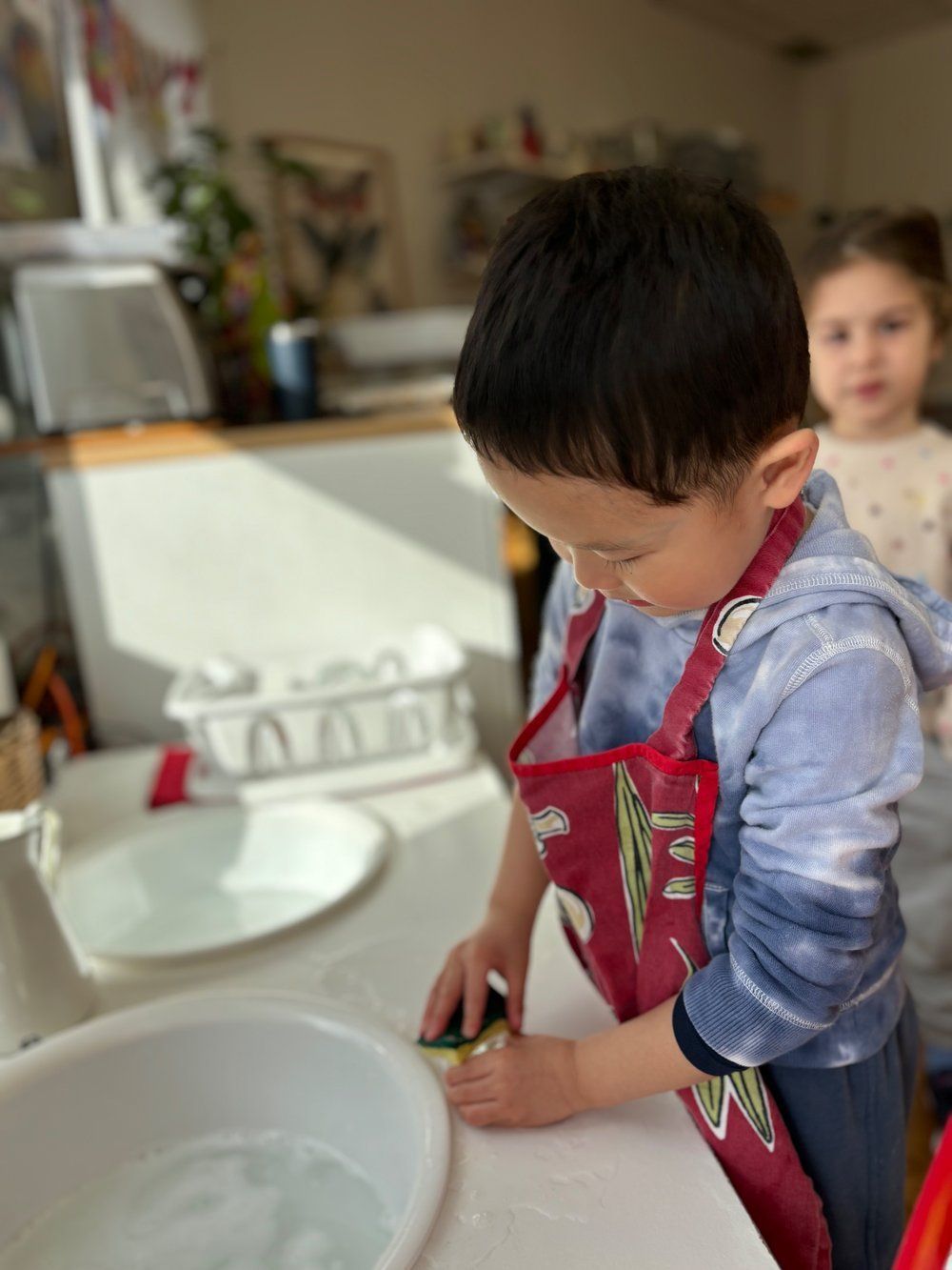 A young boy in an apron is playing with a spoon in a bowl.