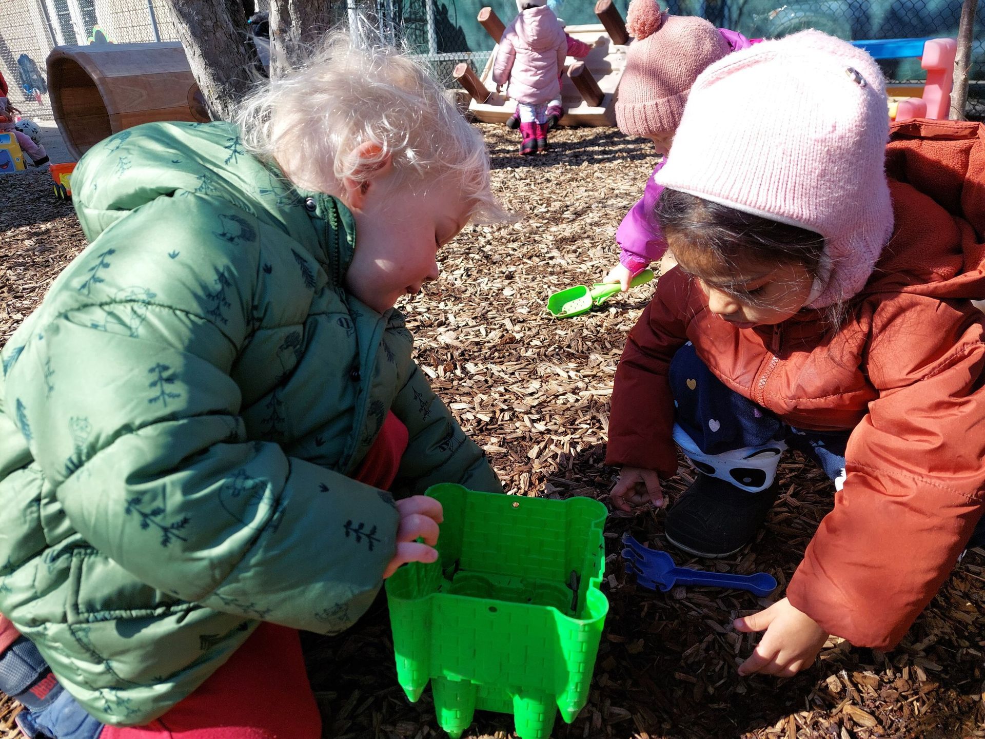 Two young children are playing in the dirt with a green sand castle.