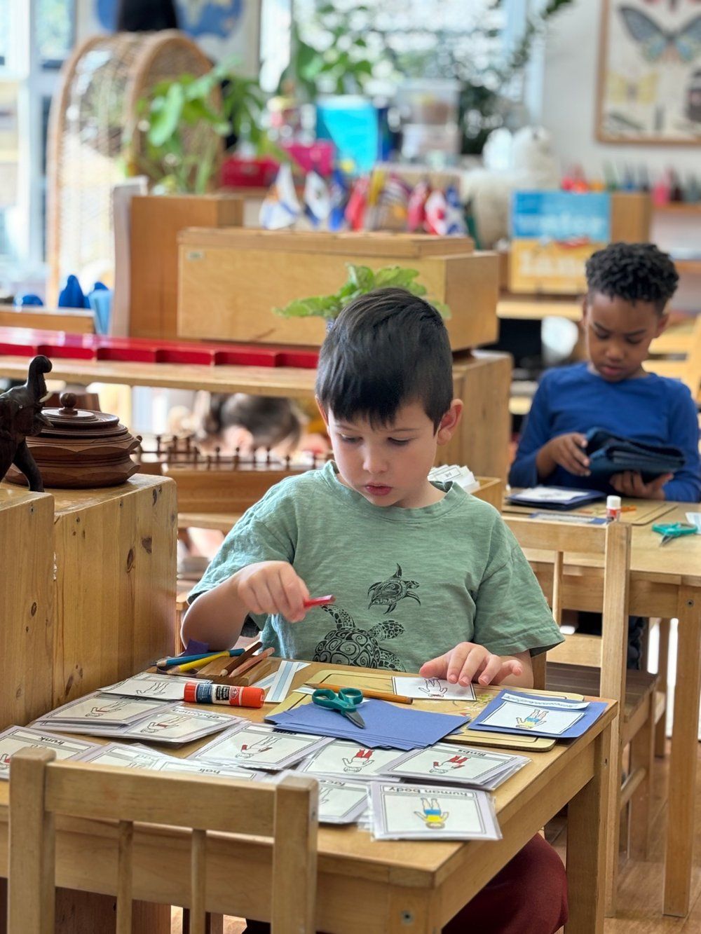 A young boy is sitting at a wooden table in a classroom.