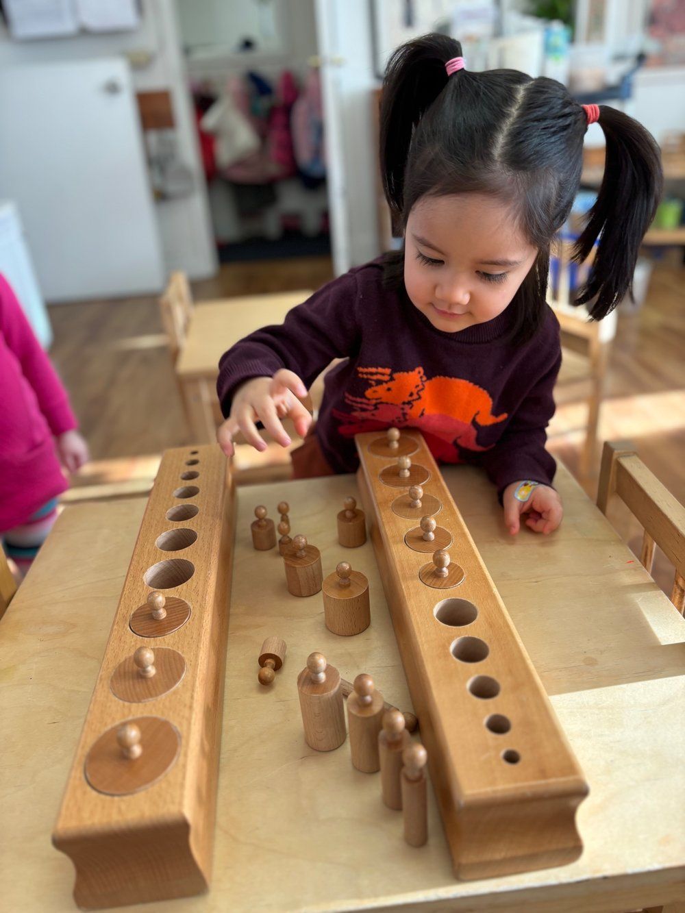 A little girl is playing with wooden blocks on a table.