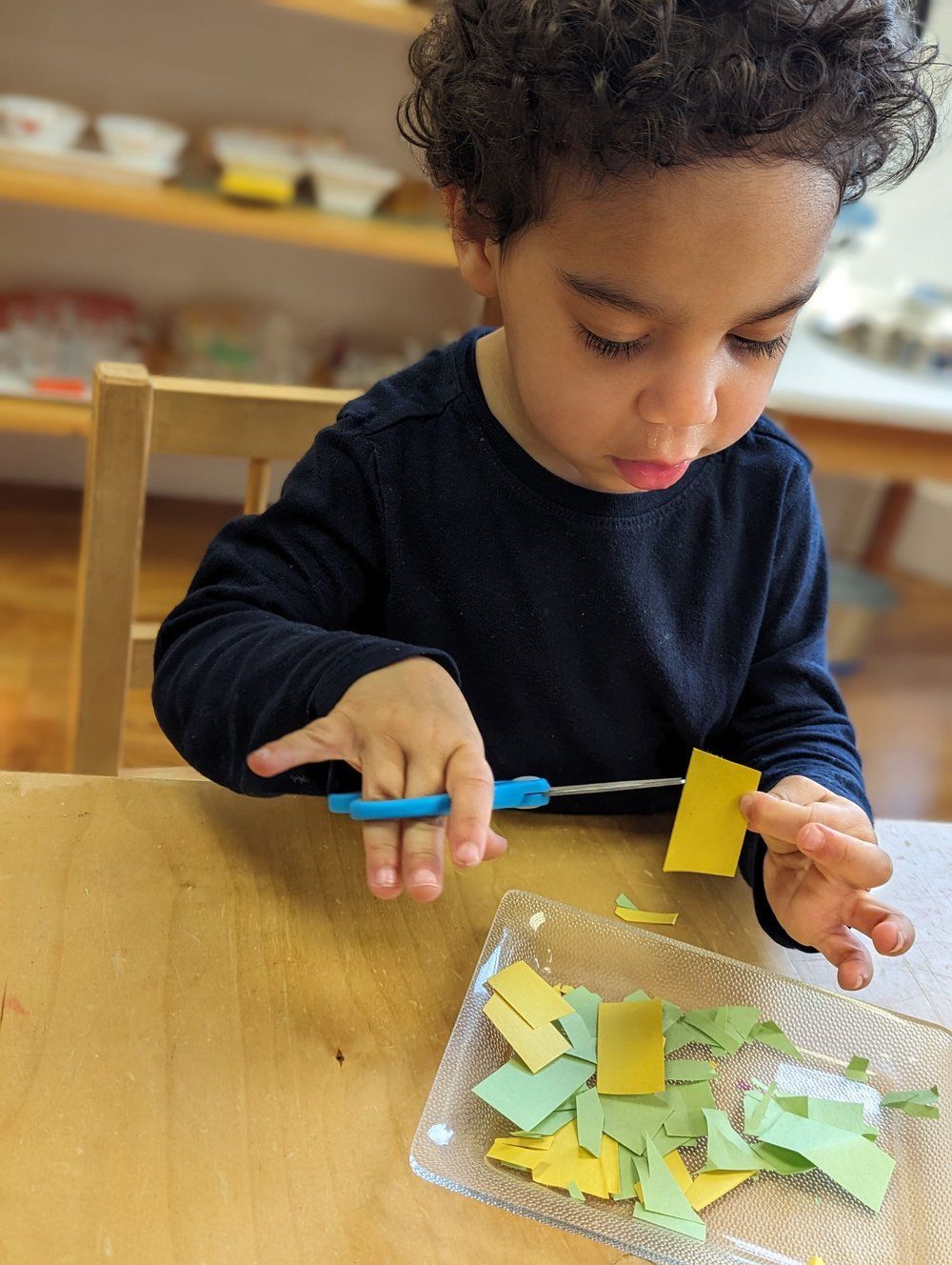 A young boy is cutting paper with scissors at a table.