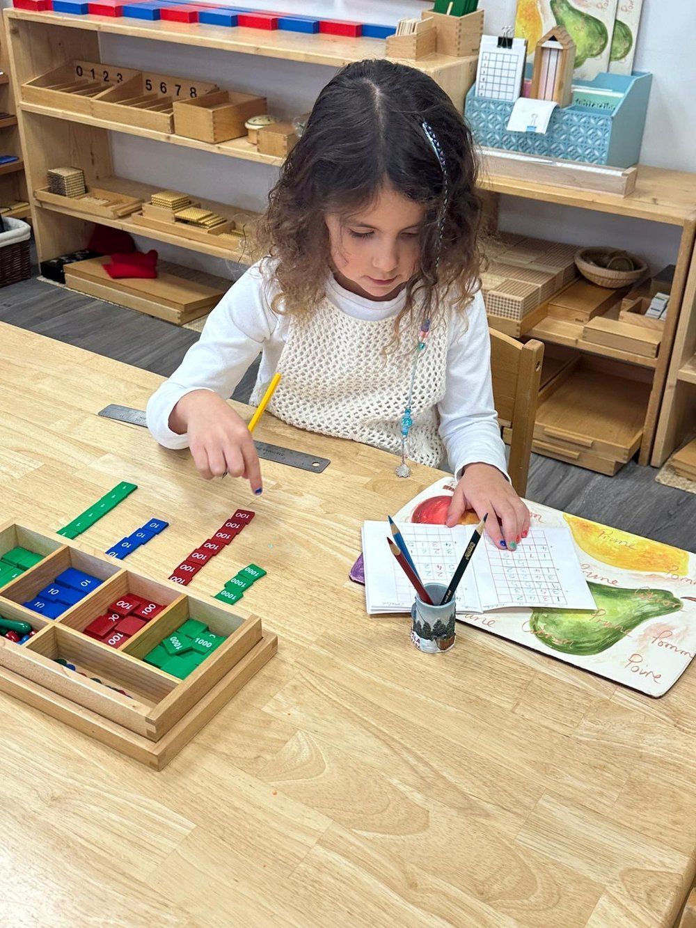 A little girl is sitting at a table playing with toys and a book.