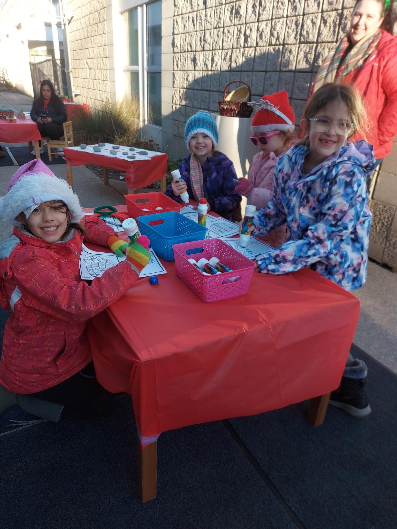 A group of children are sitting at a table with a red table cloth.