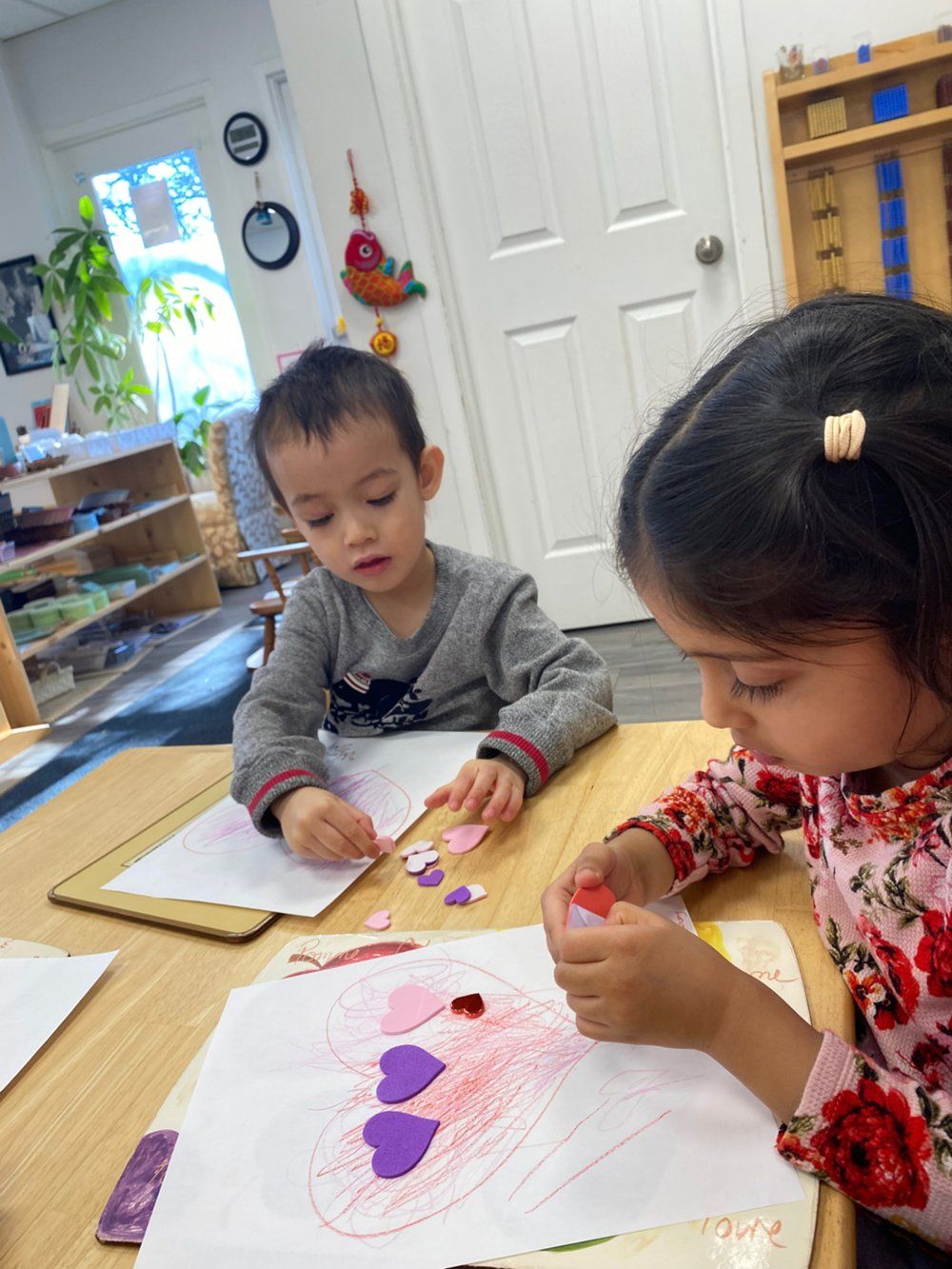 A boy and a girl are sitting at a table making valentine 's day crafts.