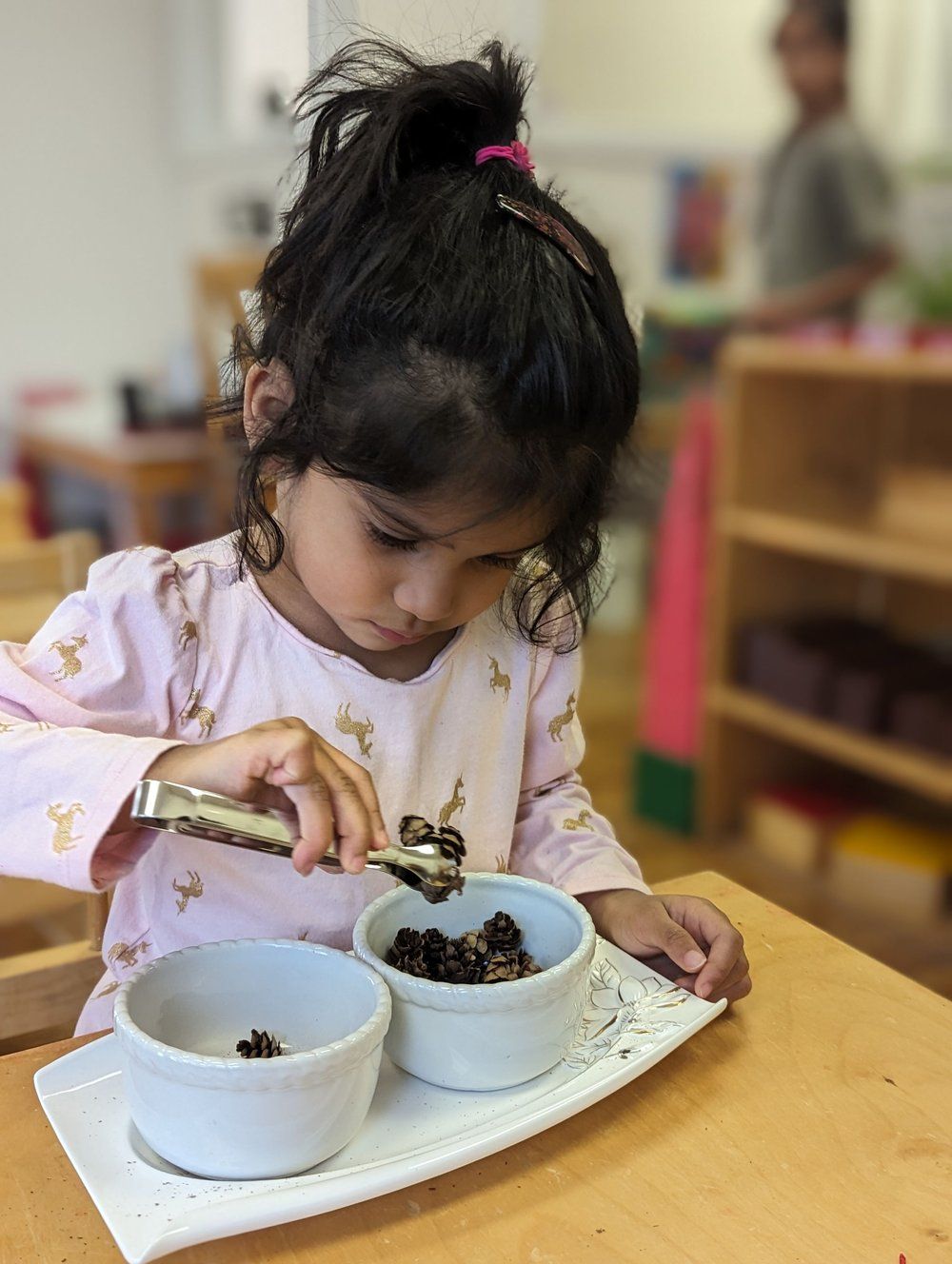 A little girl is sitting at a table playing with bowls of food.