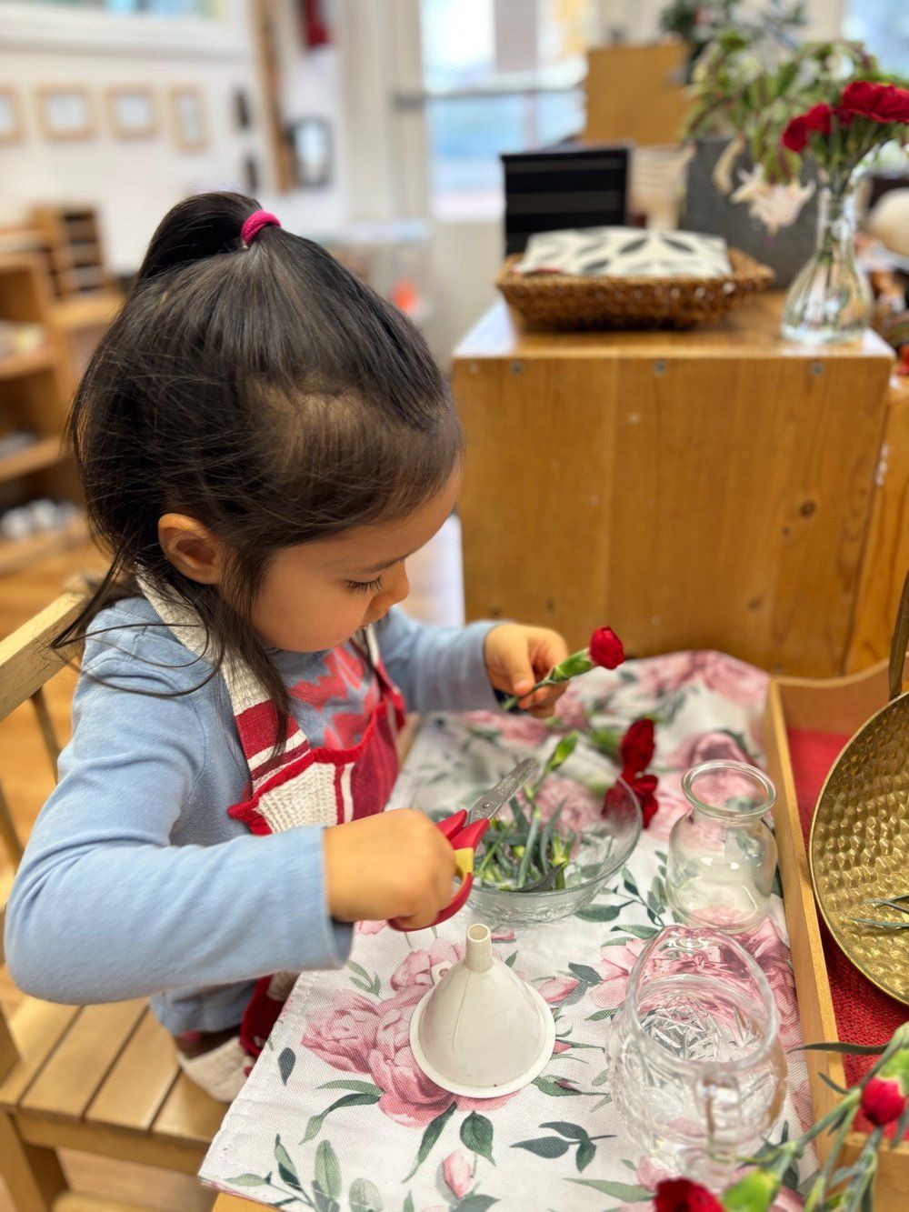 A little girl is sitting at a table playing with flowers.