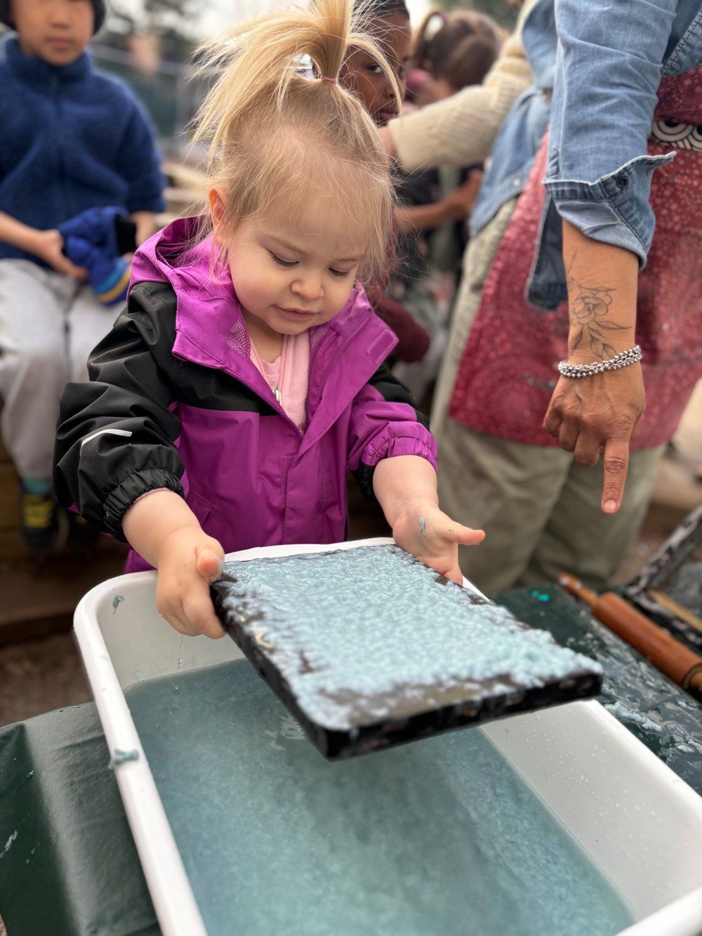 A little girl is holding a piece of paper over a tray of water.