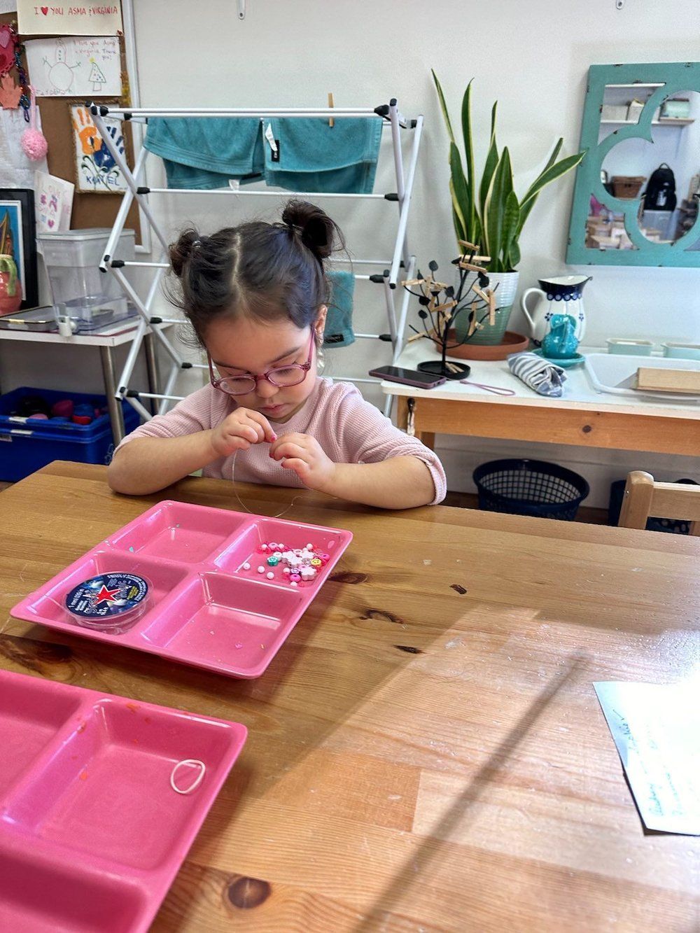 A little girl is sitting at a table with a pink tray on it.