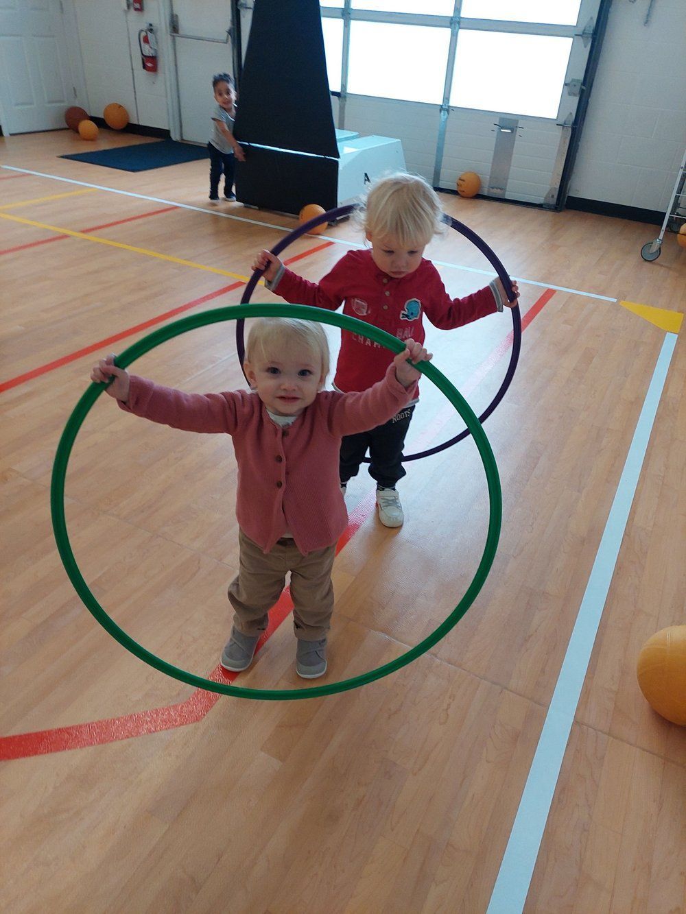 Two young children are playing with hula hoops in a gym.