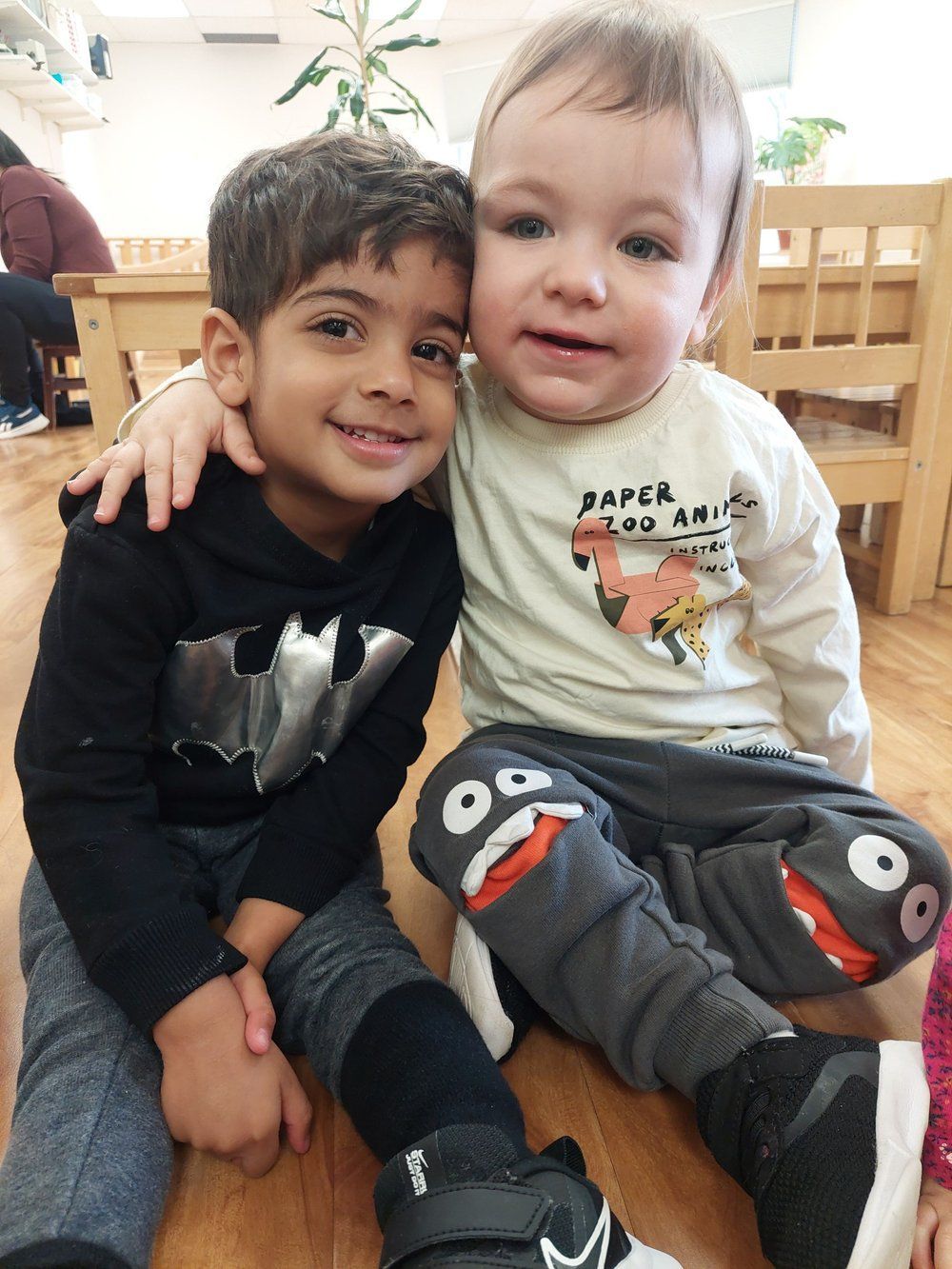 Two young boys are sitting next to each other and one has a shirt that says paper