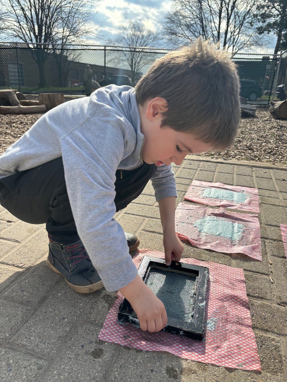 A young boy is kneeling down on a brick sidewalk playing with a tablet.