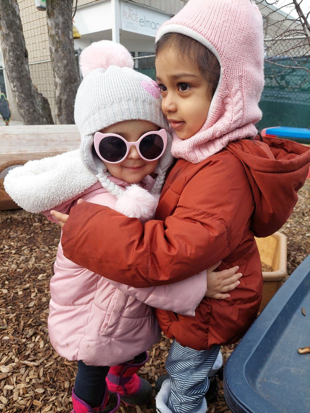 Two little girls are hugging each other while wearing sunglasses and hats.