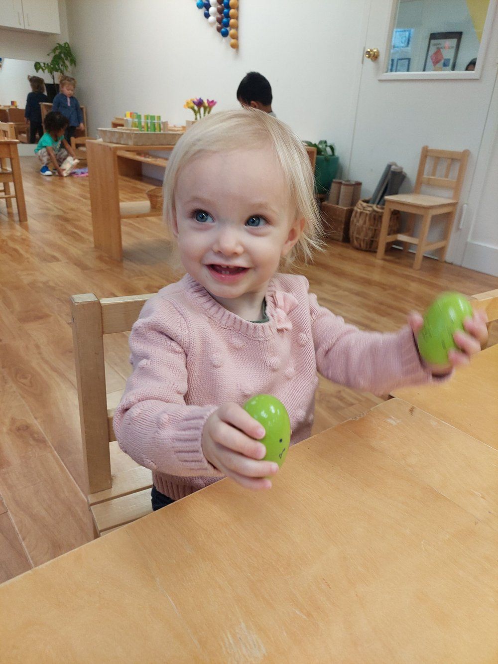 A little girl is sitting at a table holding a green ball.