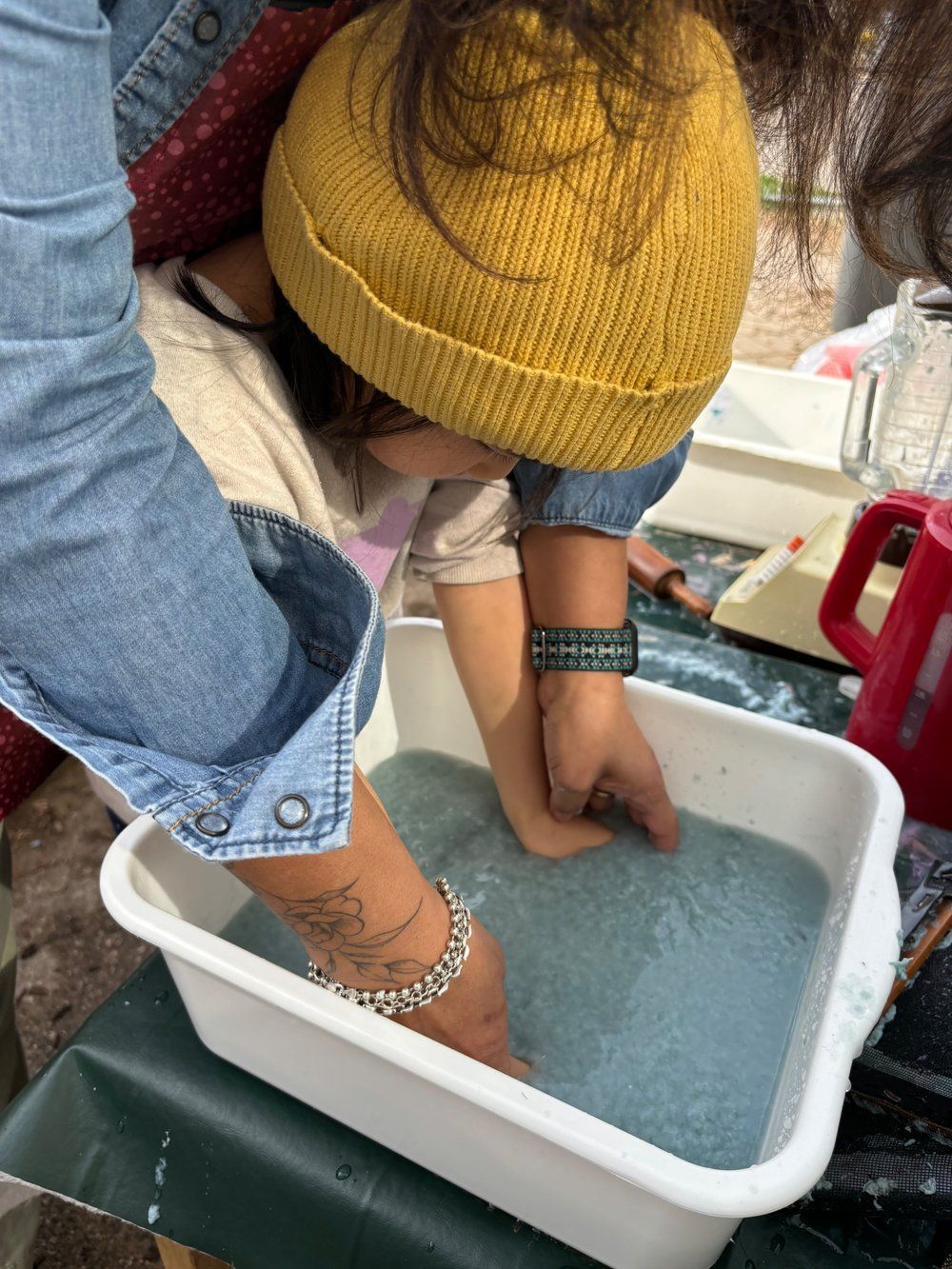 A woman is holding a child 's hand in a bowl of blue sand.