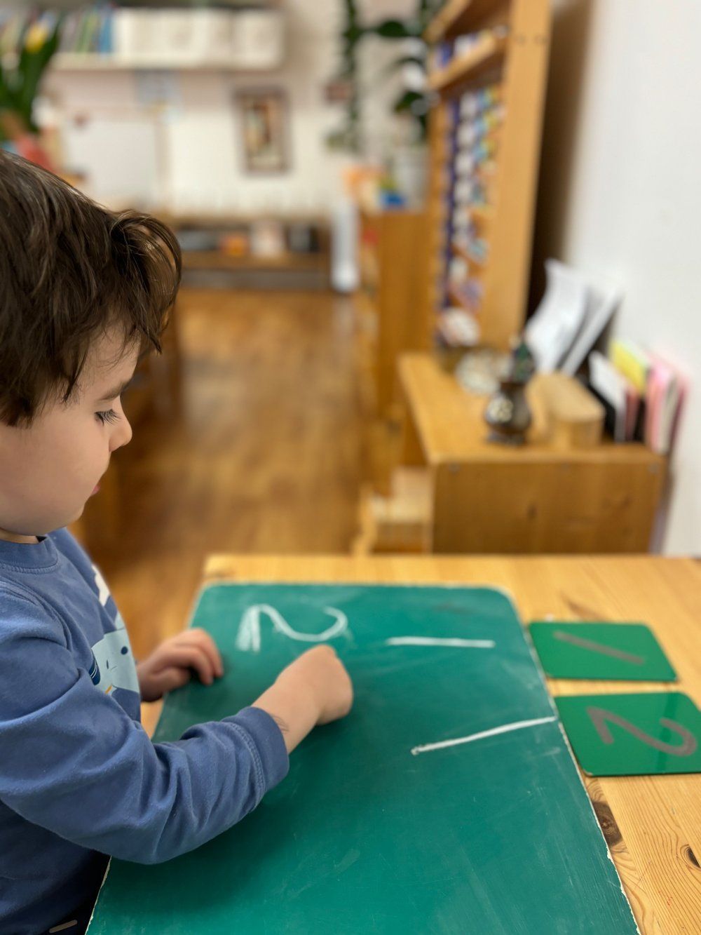 A little boy is sitting at a table playing with numbers on a chalkboard