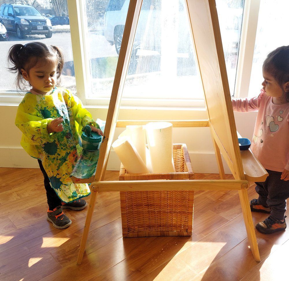 Two little girls are standing in front of an easel