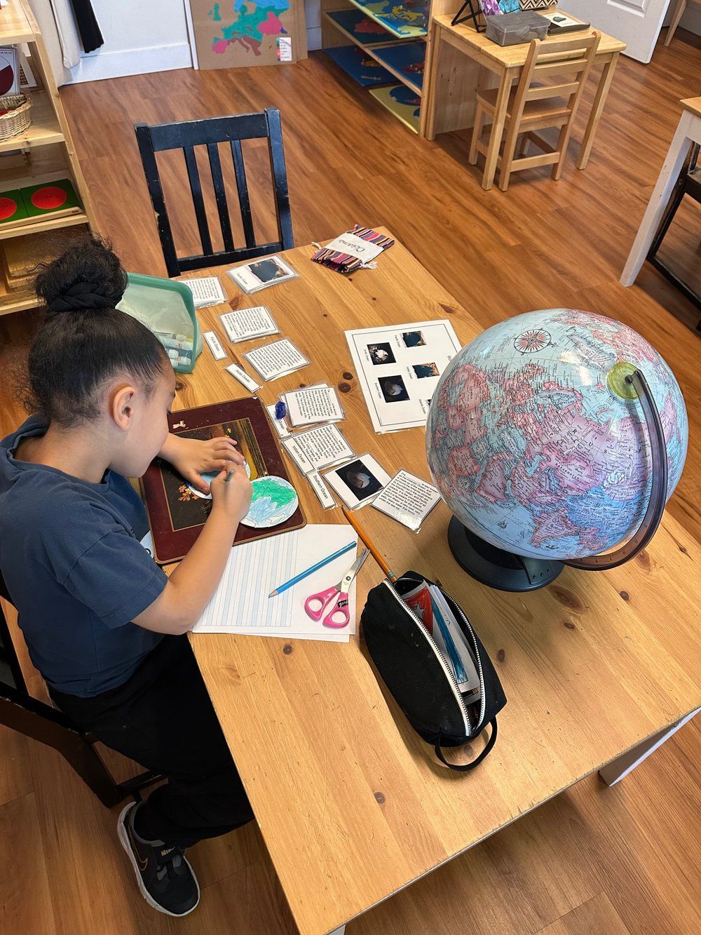 A young girl is sitting at a wooden table with a globe on it.