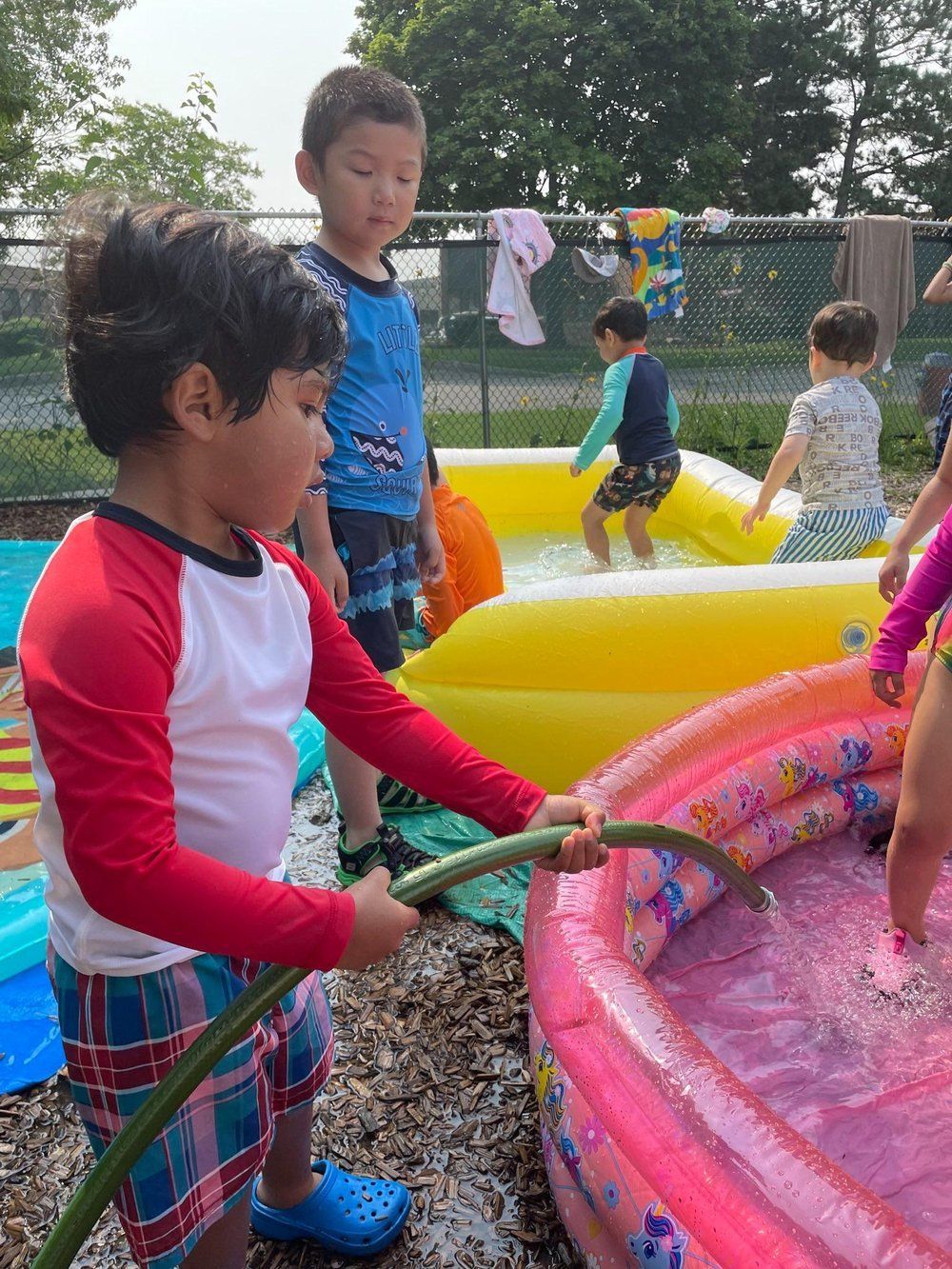 A young boy is playing with a hose in an inflatable pool.