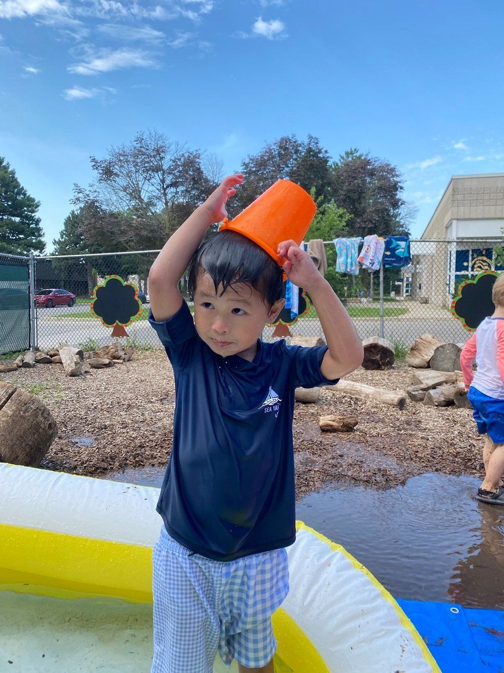 A young boy is holding an orange bucket over his head while standing in a pool.