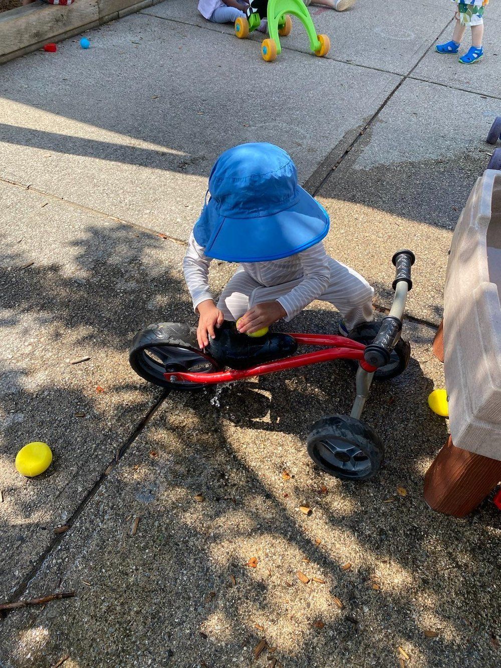 A little boy wearing a blue hat is playing with a bike on the sidewalk.