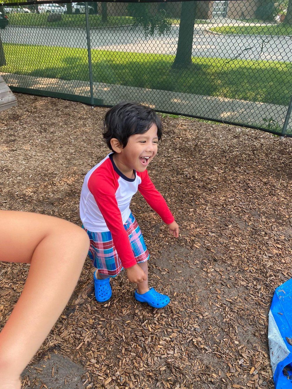 A little boy is standing in the dirt and smiling.