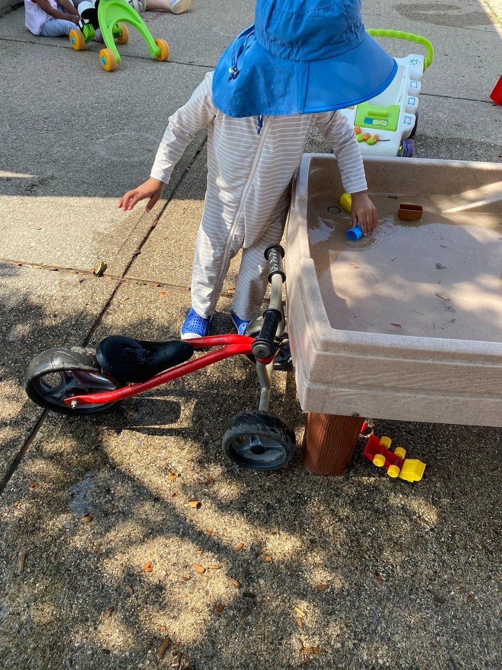 A child is standing on a bicycle next to a sandbox.