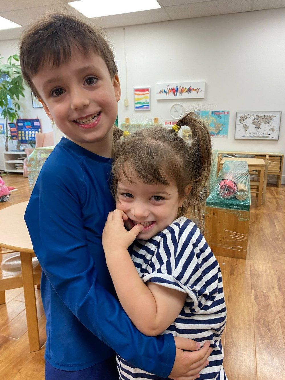 A boy and a girl are hugging each other in a classroom.