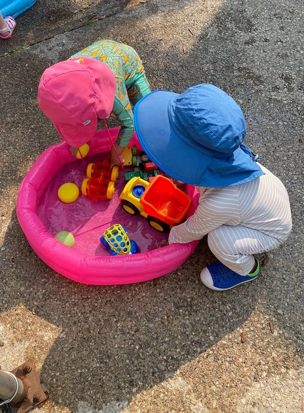 Two children are playing with toys in a pink pool.
