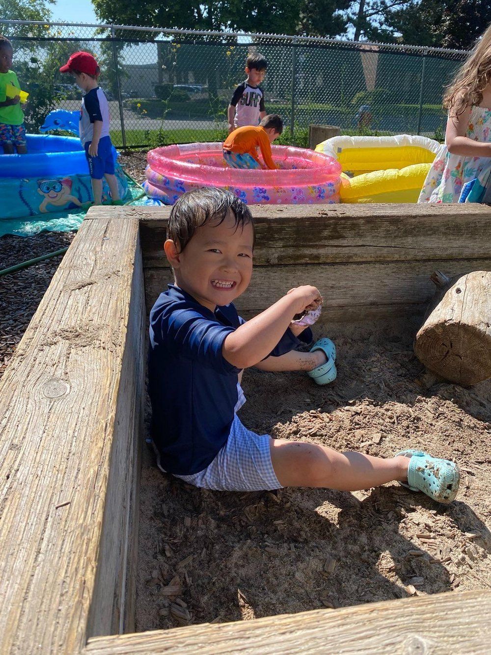 A young boy is sitting in a sandbox with other children.