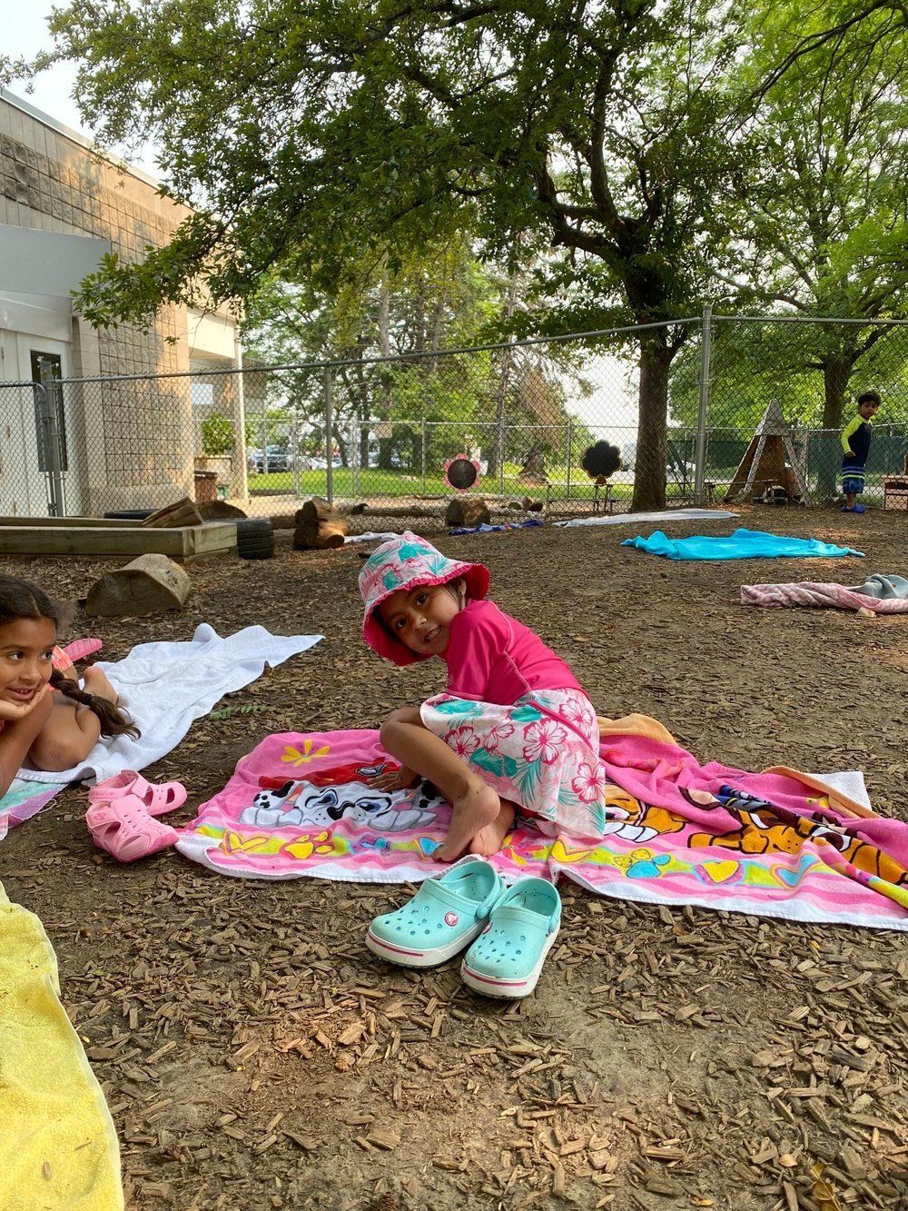 A little girl is sitting on a towel in the dirt.