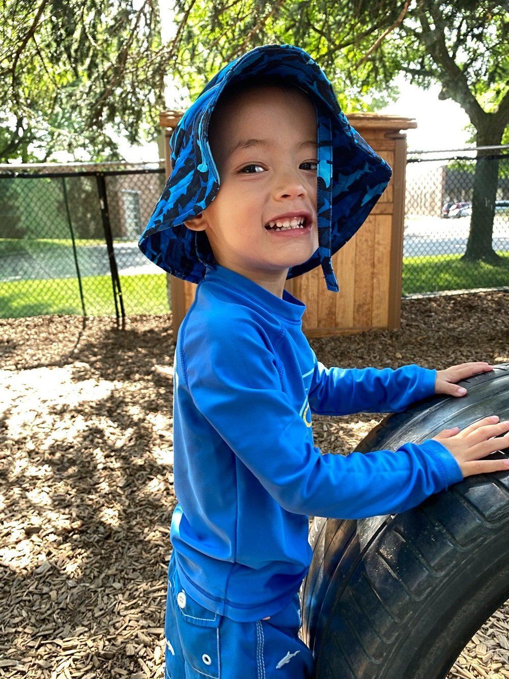 A young boy in a blue shirt and hat is playing with a tire.