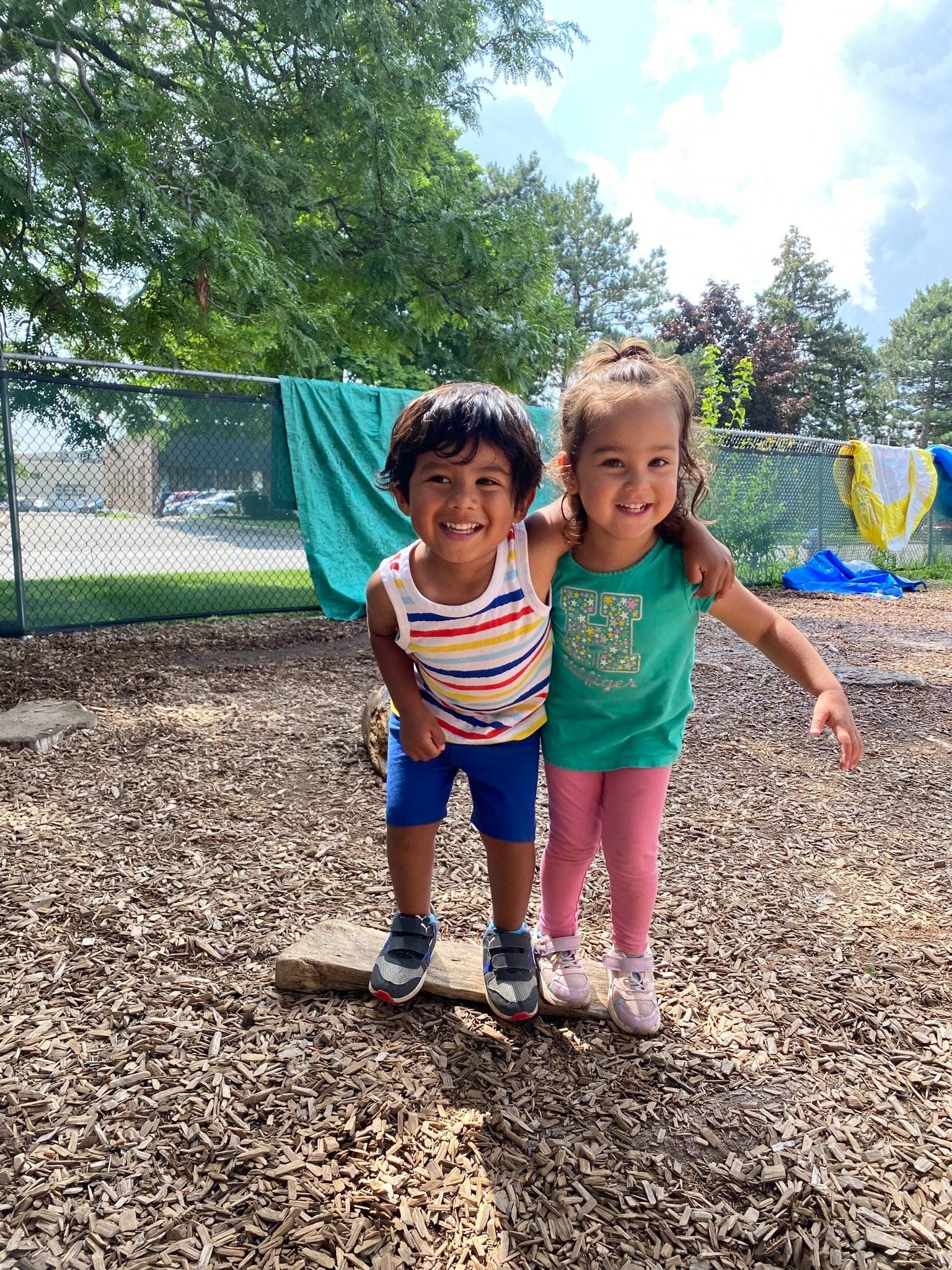 A boy and a girl are standing next to each other in a playground.